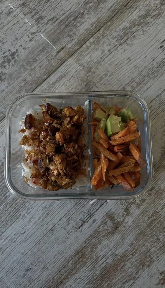 Een voorbereide maaltijd in een glazen doos: kip met rijst, zoete aardappel en avocado