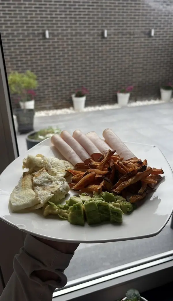 Een ontbijtbord met omelet, hesp, avocado en zoete aardappel